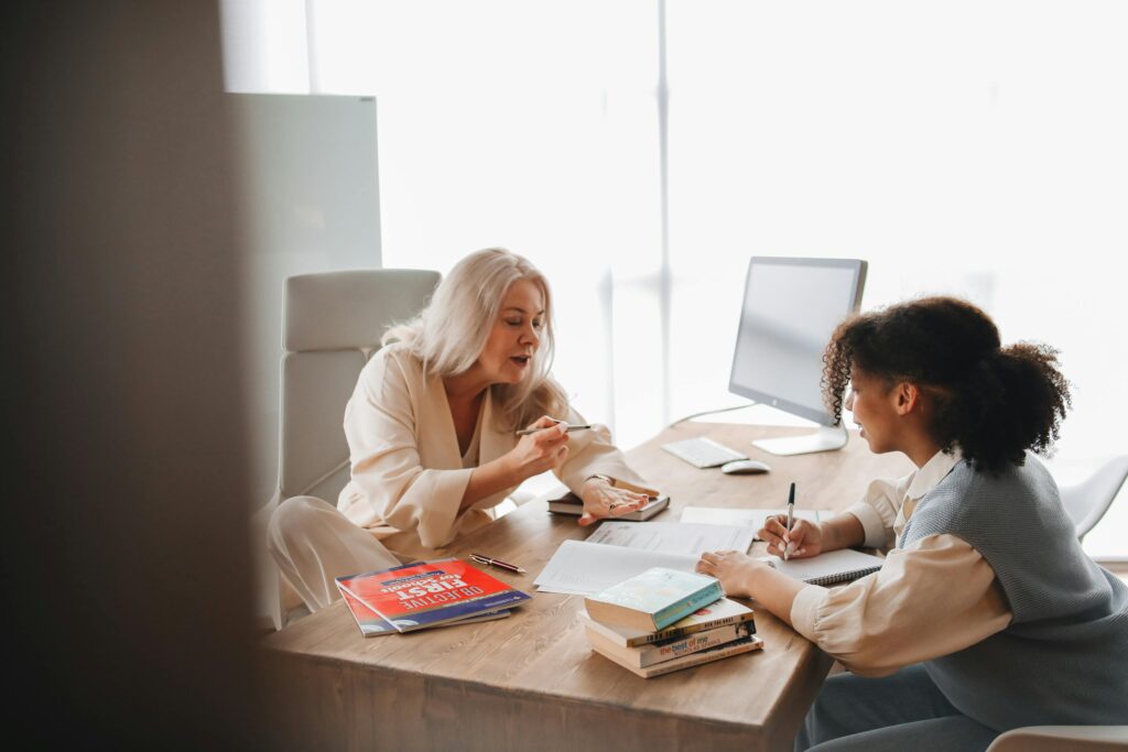 Educator explains concepts to a student in a classroom environment with books and notes.
