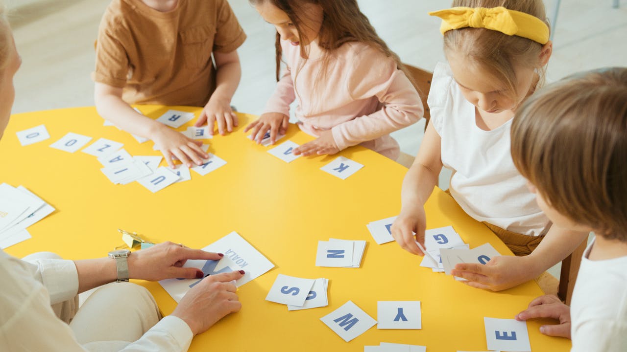 Group of children engaging with alphabet cards on a bright yellow table for learning.